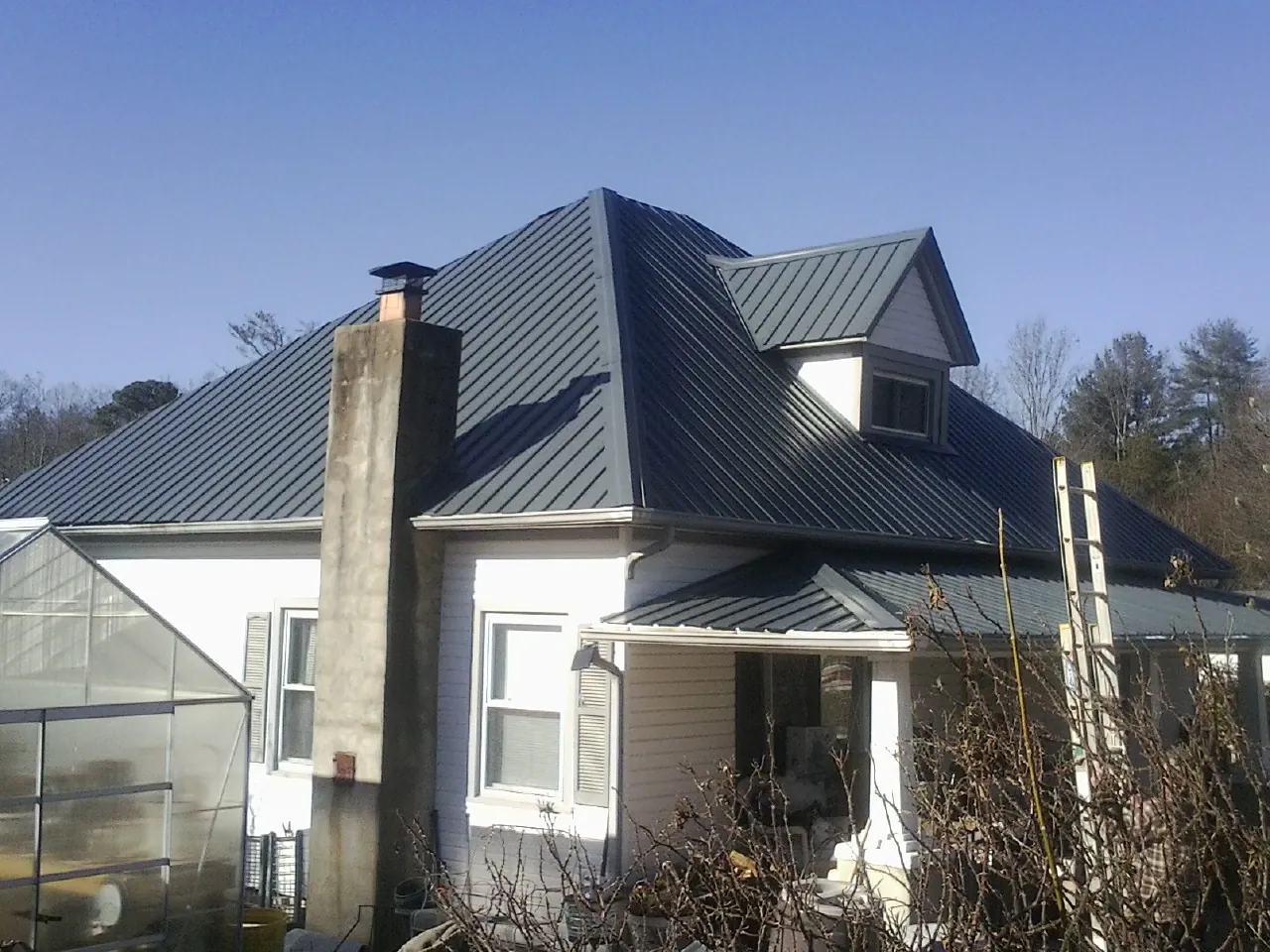 Dark blue standing seam metal roof on a white farmhouse with dormer — Slate & Tile Roof Repair by Roofing Brothers in Bountiful