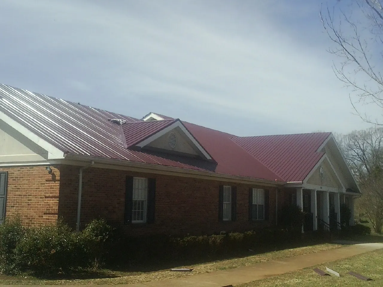 Red metal roof with gabled entries on a long brick building, from a Hail Damage Roof Repair job in Bountiful