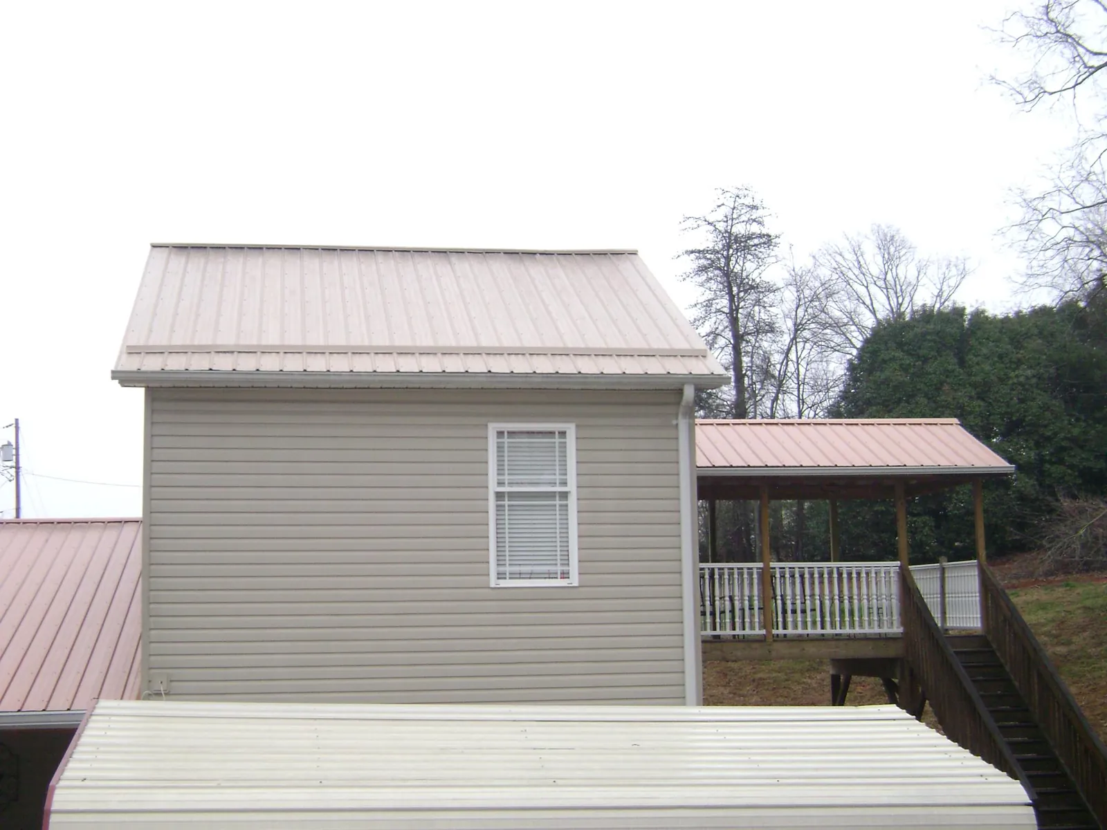 Tan metal roofs on a two story addition and attached porch, from a Roof Replacement job in Bountiful